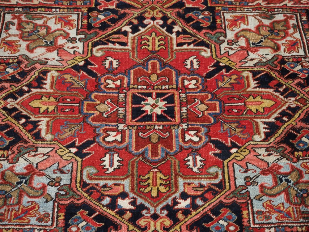 An antique hand-knotted wool Heriz carpet featuring a large central geometric medallion in rust red, navy blue, and cream surrounded by detailed geometric borders. View XIII