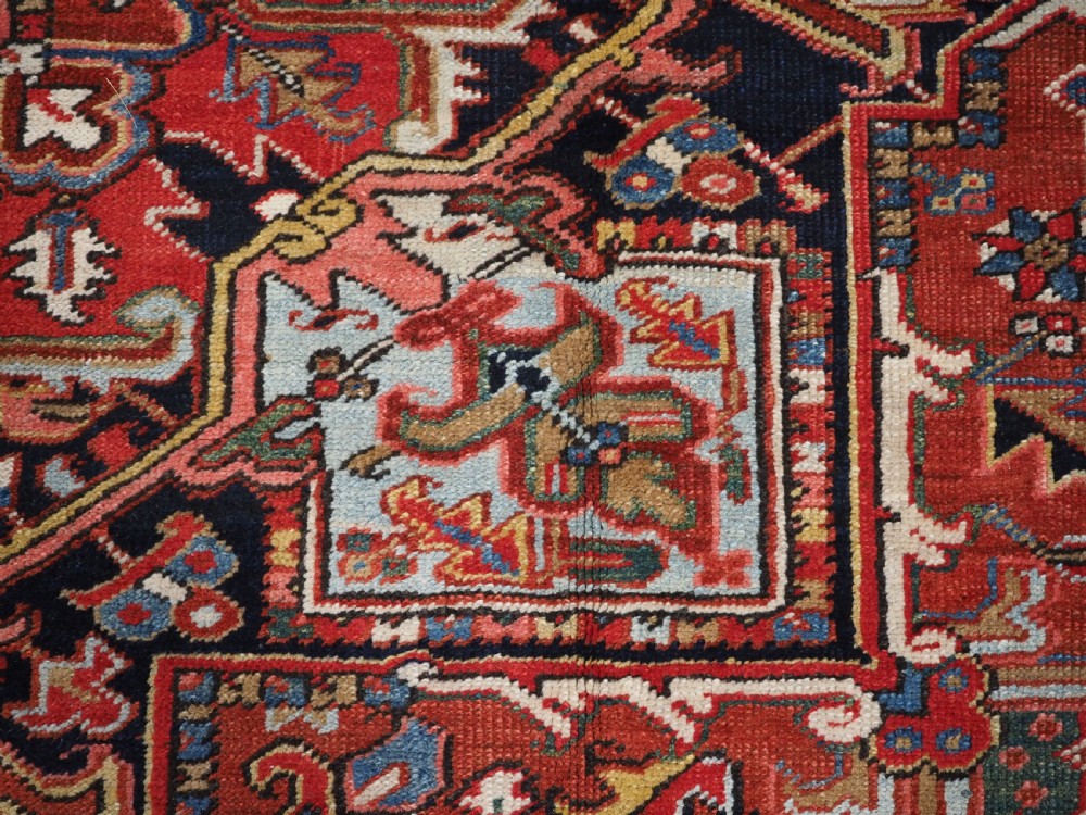 An antique hand-knotted wool Heriz carpet featuring a large central geometric medallion in rust red, navy blue, and cream surrounded by detailed geometric borders. View XIV