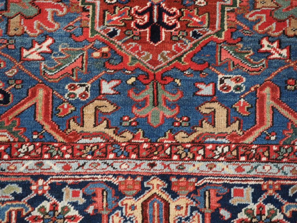 An antique hand-knotted wool Heriz carpet featuring a large central geometric medallion in rust red, navy blue, and cream surrounded by detailed geometric borders. View XVI