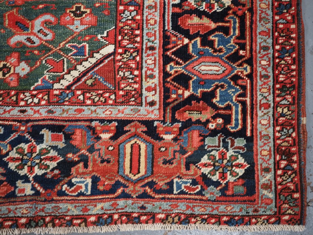 An antique hand-knotted wool Heriz carpet featuring a large central geometric medallion in rust red, navy blue, and cream surrounded by detailed geometric borders. View XVII