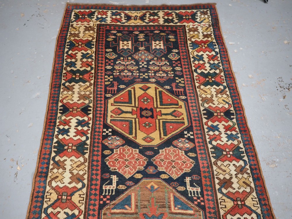 A long antique hand-knotted Caucasian wool runner rug featuring repeating geometric medallions in red, navy blue, ochre, and cream. View II