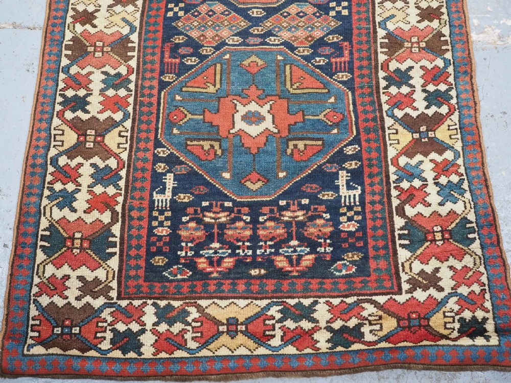 A long antique hand-knotted Caucasian wool runner rug featuring repeating geometric medallions in red, navy blue, ochre, and cream. View V