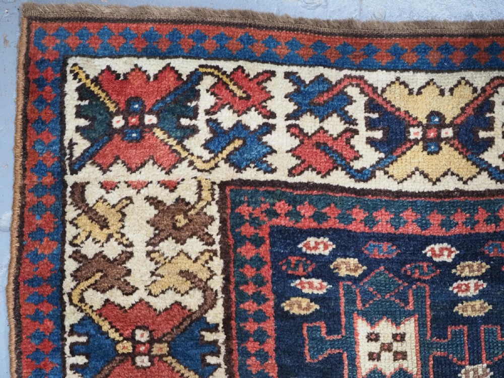 A long antique hand-knotted Caucasian wool runner rug featuring repeating geometric medallions in red, navy blue, ochre, and cream. View VI