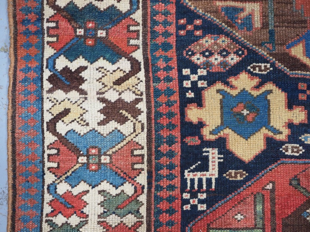 A long antique hand-knotted Caucasian wool runner rug featuring repeating geometric medallions in red, navy blue, ochre, and cream. View VII