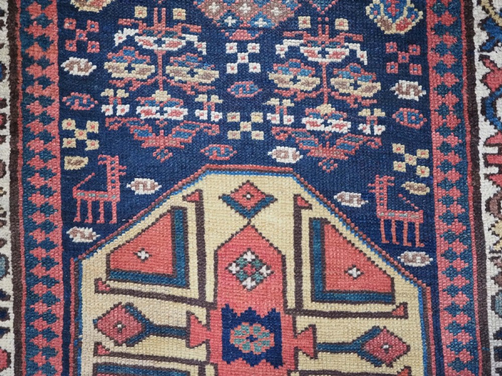 A long antique hand-knotted Caucasian wool runner rug featuring repeating geometric medallions in red, navy blue, ochre, and cream. View VIII