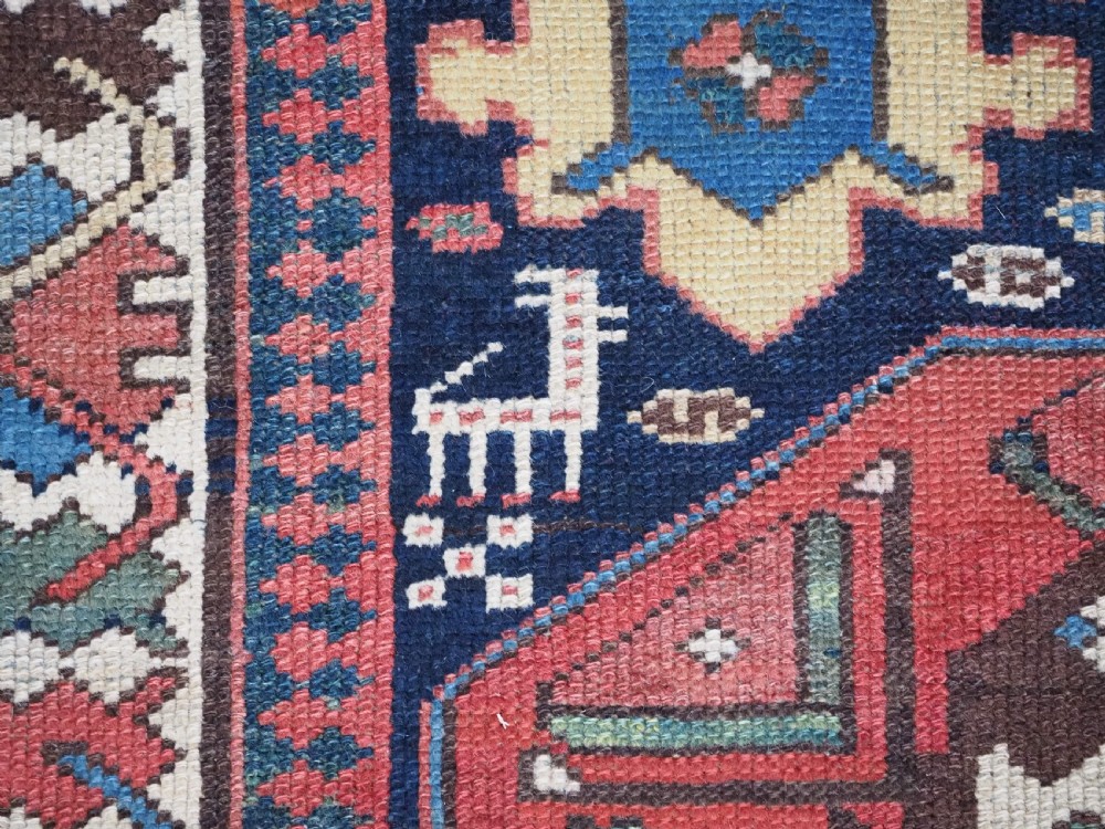 A long antique hand-knotted Caucasian wool runner rug featuring repeating geometric medallions in red, navy blue, ochre, and cream. View X