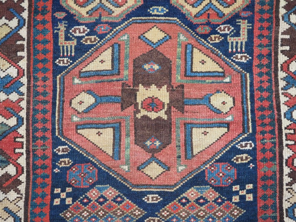 A long antique hand-knotted Caucasian wool runner rug featuring repeating geometric medallions in red, navy blue, ochre, and cream. View XI