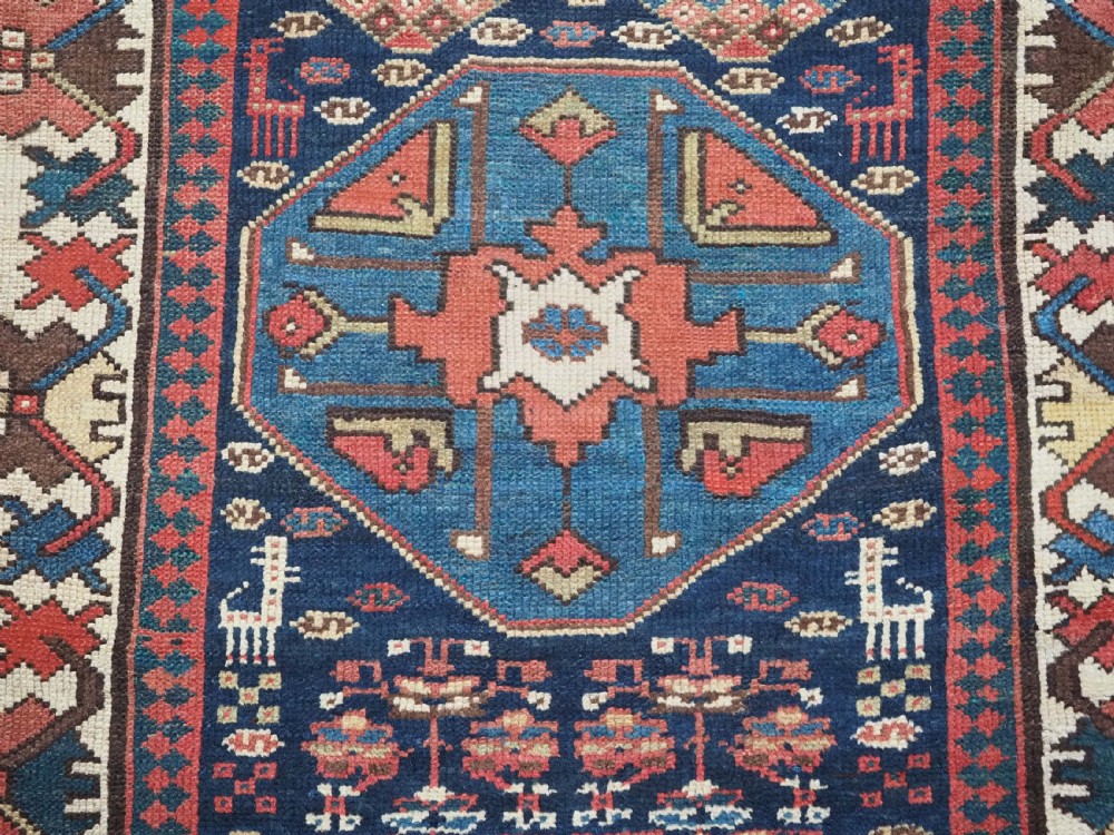A long antique hand-knotted Caucasian wool runner rug featuring repeating geometric medallions in red, navy blue, ochre, and cream. View XII