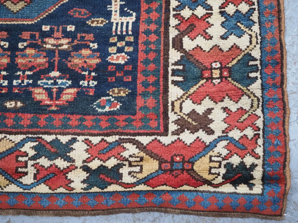 A long antique hand-knotted Caucasian wool runner rug featuring repeating geometric medallions in red, navy blue, ochre, and cream. View XIII