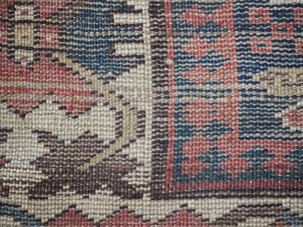 A long antique hand-knotted Caucasian wool runner rug featuring repeating geometric medallions in red, navy blue, ochre, and cream. View XIV