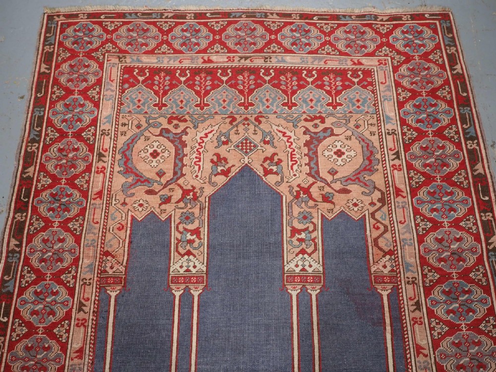 A hand-knotted wool prayer rug with a blue central column niche motif framed by beige spandrels and a red geometric border. View III