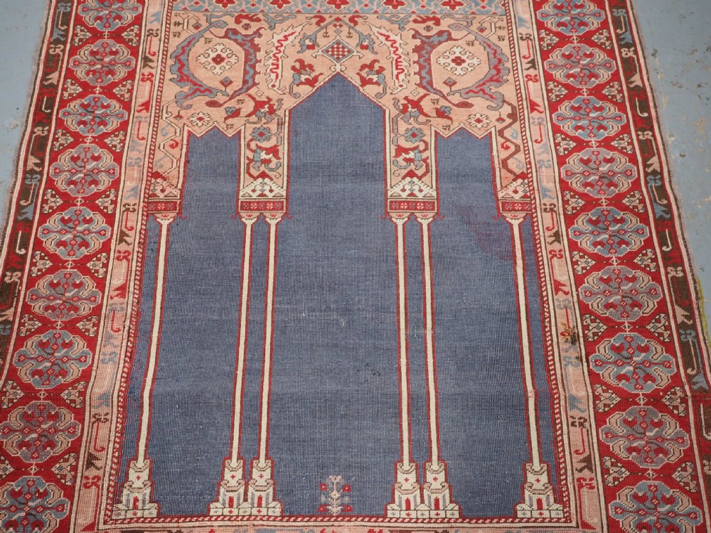 A hand-knotted wool prayer rug with a blue central column niche motif framed by beige spandrels and a red geometric border. View IV