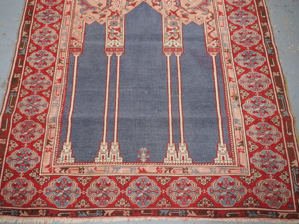 A hand-knotted wool prayer rug with a blue central column niche motif framed by beige spandrels and a red geometric border. View V