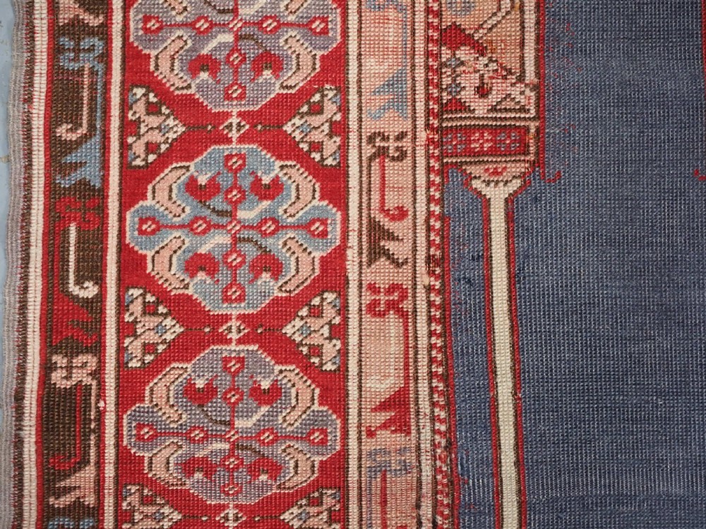 A hand-knotted wool prayer rug with a blue central column niche motif framed by beige spandrels and a red geometric border. View VII