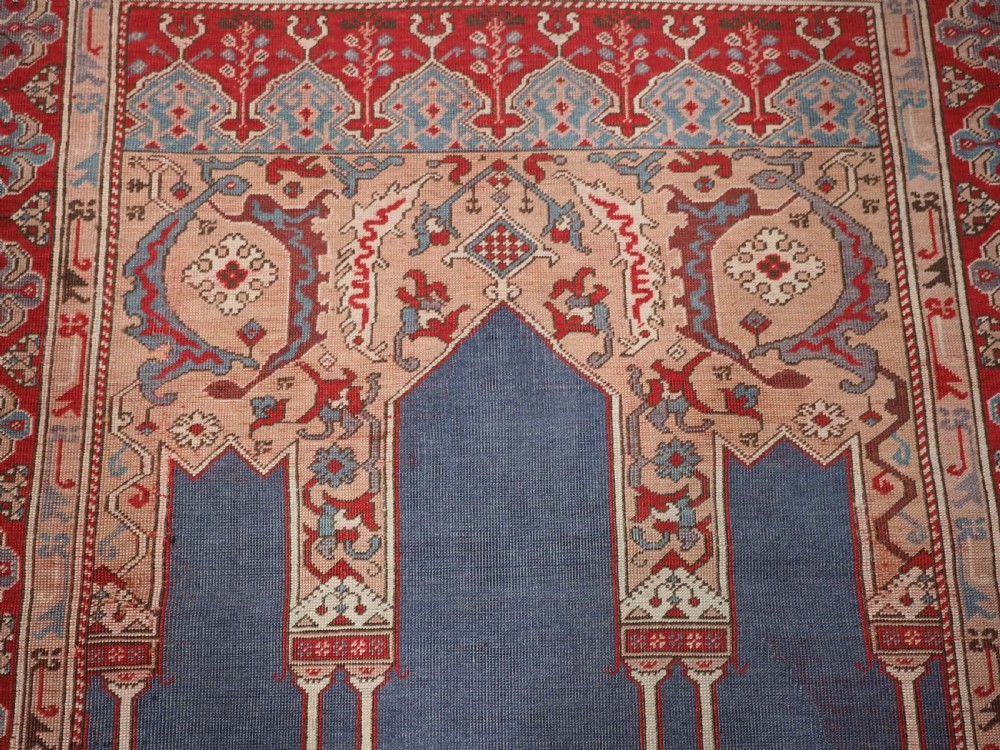 A hand-knotted wool prayer rug with a blue central column niche motif framed by beige spandrels and a red geometric border. View VIII