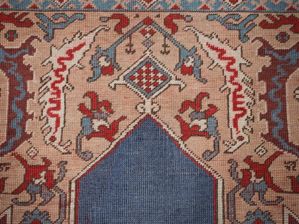 A hand-knotted wool prayer rug with a blue central column niche motif framed by beige spandrels and a red geometric border. View X