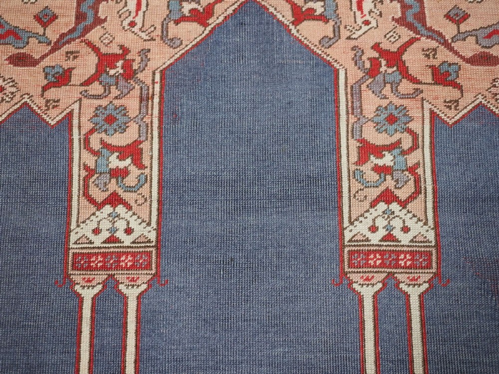 A hand-knotted wool prayer rug with a blue central column niche motif framed by beige spandrels and a red geometric border. View XII