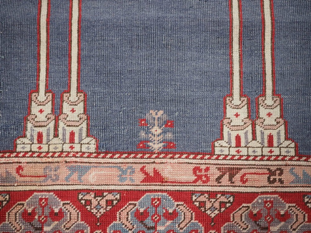 A hand-knotted wool prayer rug with a blue central column niche motif framed by beige spandrels and a red geometric border. View XIII