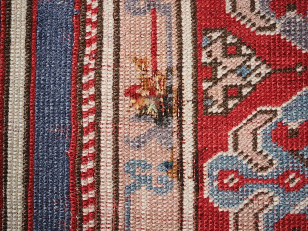 A hand-knotted wool prayer rug with a blue central column niche motif framed by beige spandrels and a red geometric border. View XVII