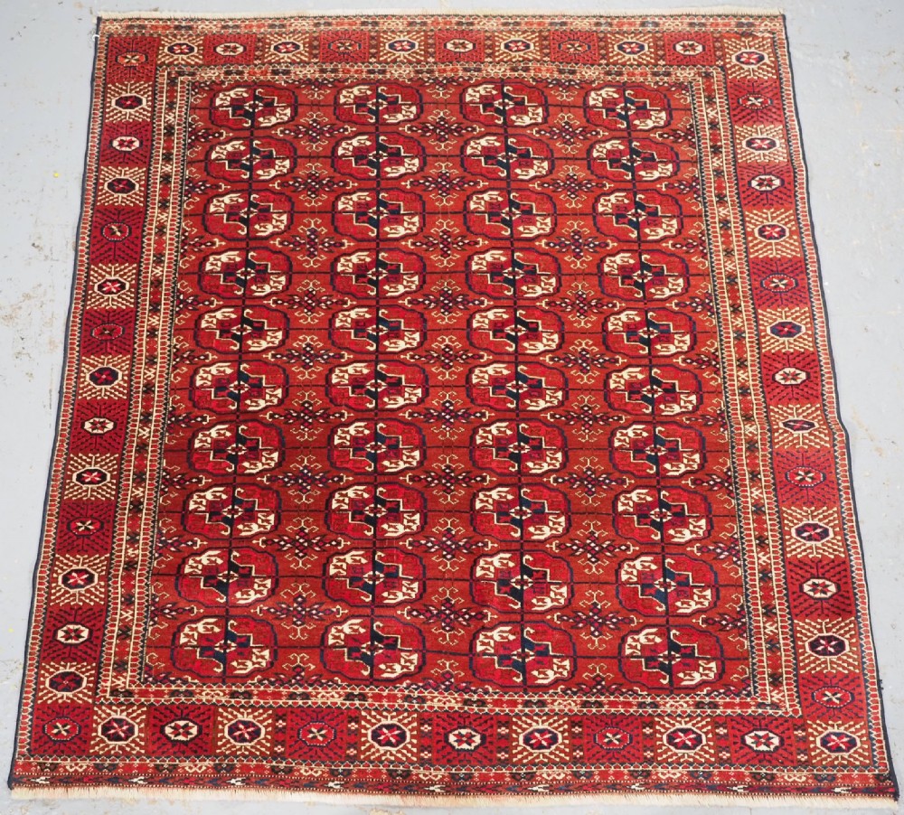 A rectangular hand-knotted Tekke Turkmen wool rug featuring repeated geometric primary guls on a deep red field surrounded by multi-band borders.