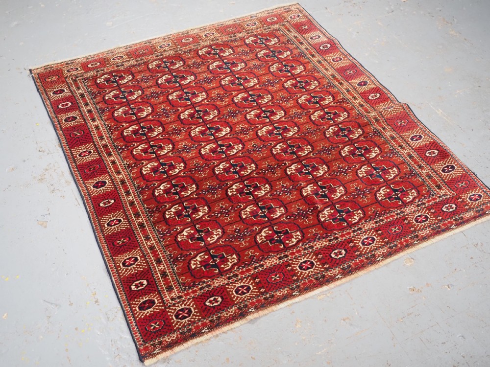 A rectangular hand-knotted Tekke Turkmen wool rug featuring repeated geometric primary guls on a deep red field surrounded by multi-band borders. View II
