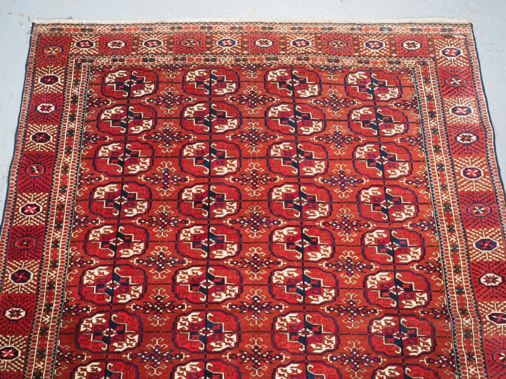 A rectangular hand-knotted Tekke Turkmen wool rug featuring repeated geometric primary guls on a deep red field surrounded by multi-band borders. View III
