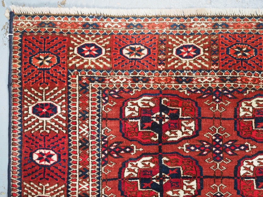A rectangular hand-knotted Tekke Turkmen wool rug featuring repeated geometric primary guls on a deep red field surrounded by multi-band borders. View V