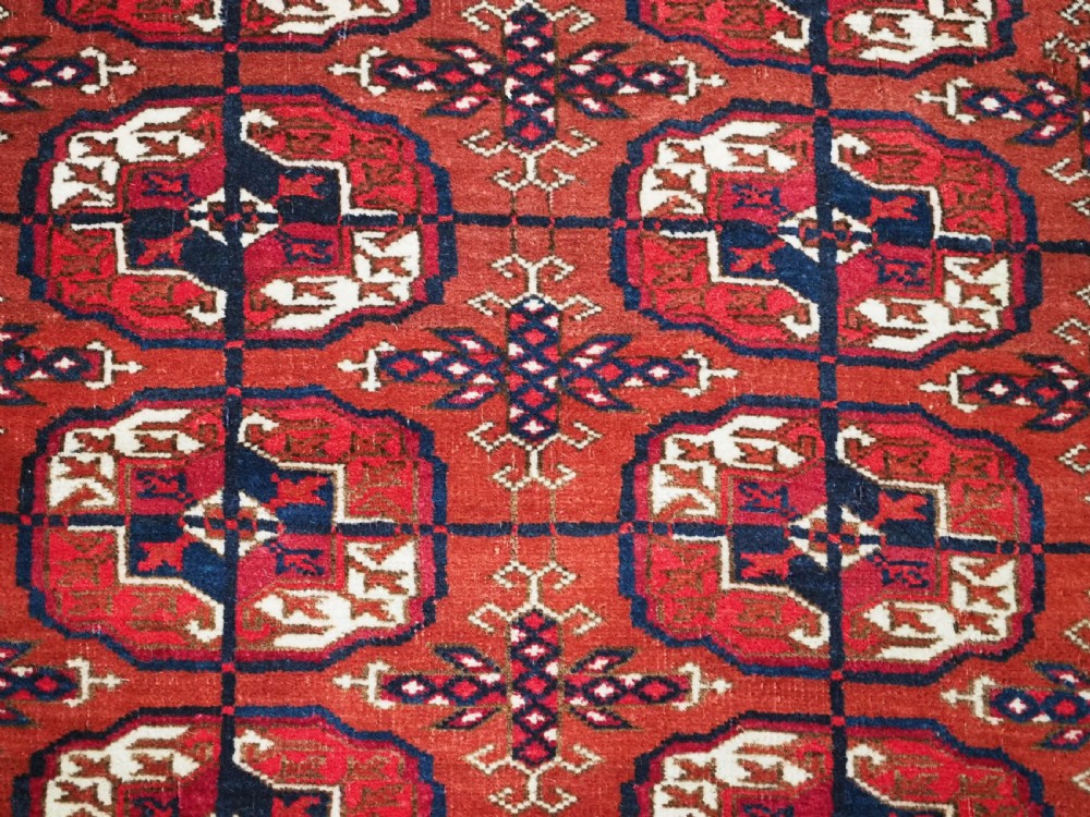 A rectangular hand-knotted Tekke Turkmen wool rug featuring repeated geometric primary guls on a deep red field surrounded by multi-band borders. View VII