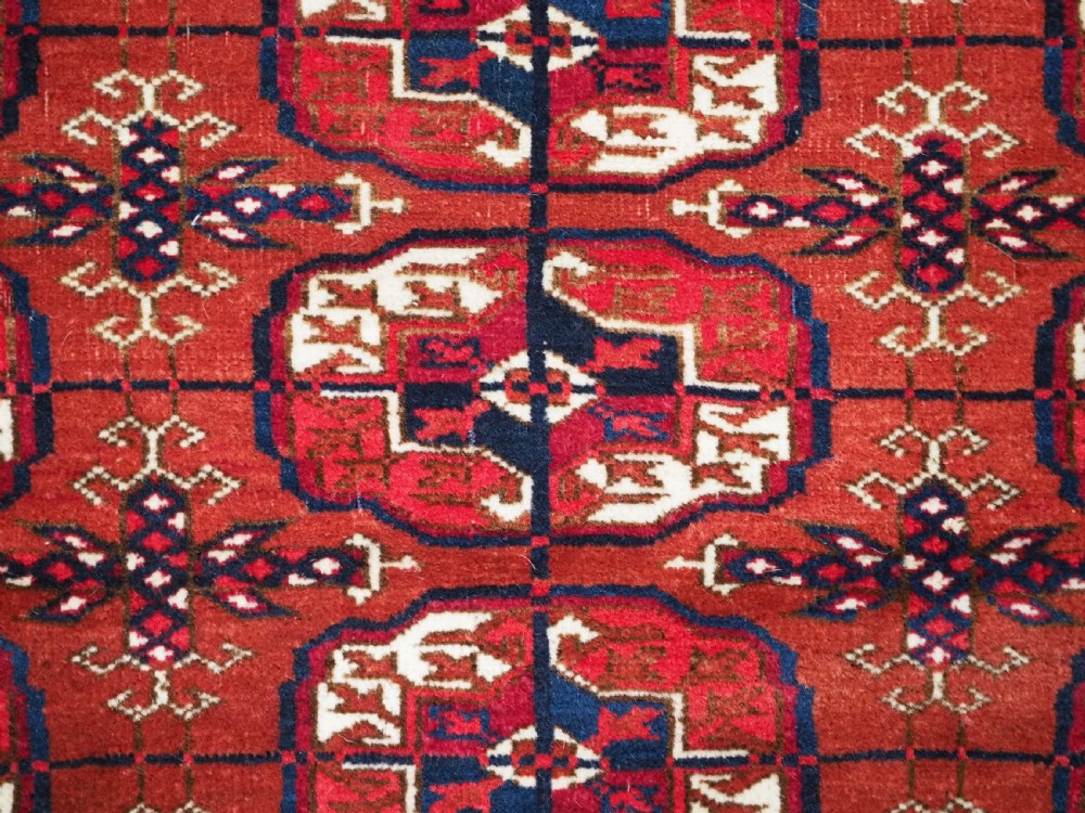 A rectangular hand-knotted Tekke Turkmen wool rug featuring repeated geometric primary guls on a deep red field surrounded by multi-band borders. View VIII