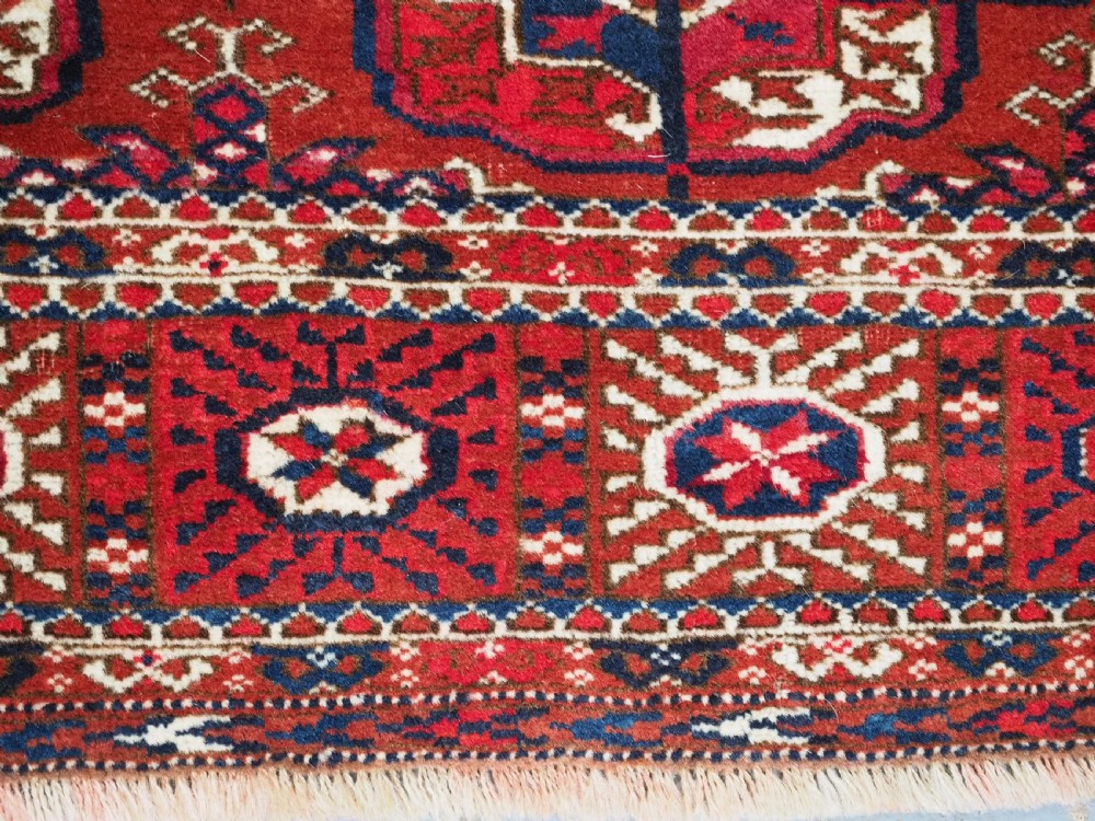 A rectangular hand-knotted Tekke Turkmen wool rug featuring repeated geometric primary guls on a deep red field surrounded by multi-band borders. View IX
