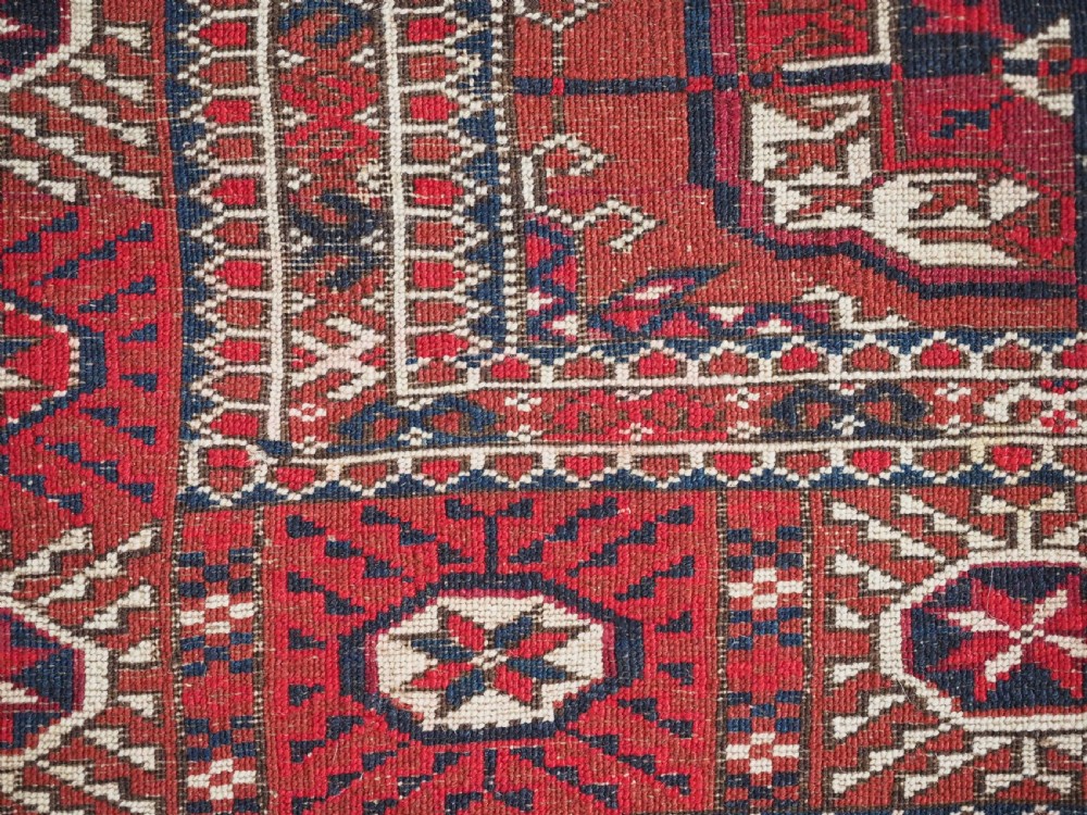 A rectangular hand-knotted Tekke Turkmen wool rug featuring repeated geometric primary guls on a deep red field surrounded by multi-band borders. View XI