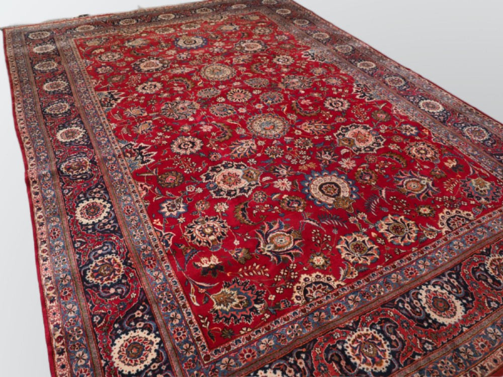 A large hand-knotted Kashan wool carpet featuring an intricate all-over floral pattern on a rich red field framed by a navy blue patterned border. View II
