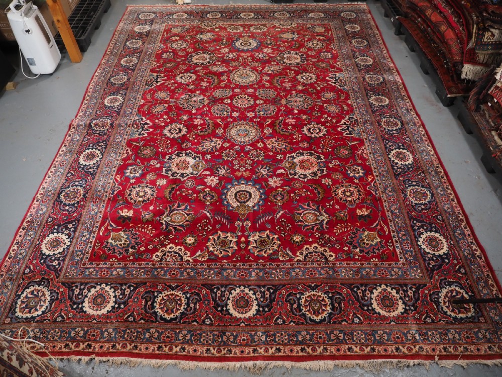 A large hand-knotted Kashan wool carpet featuring an intricate all-over floral pattern on a rich red field framed by a navy blue patterned border. View III