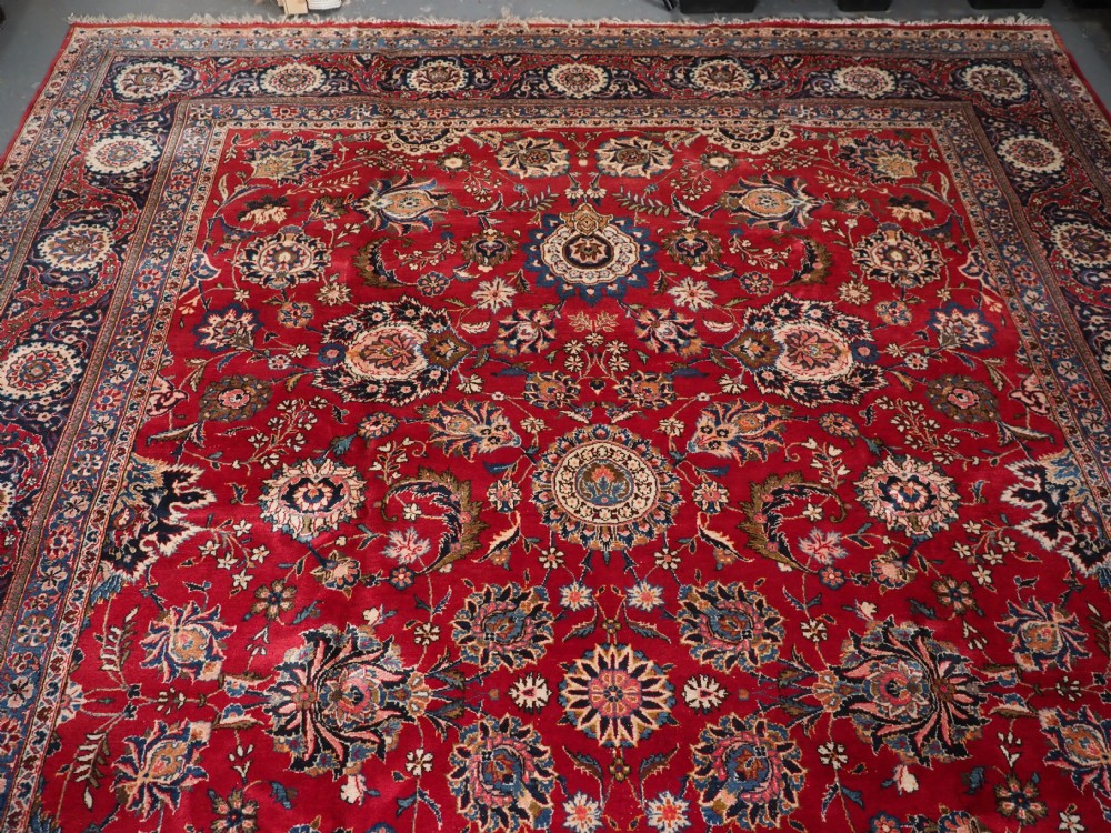 A large hand-knotted Kashan wool carpet featuring an intricate all-over floral pattern on a rich red field framed by a navy blue patterned border. View IV