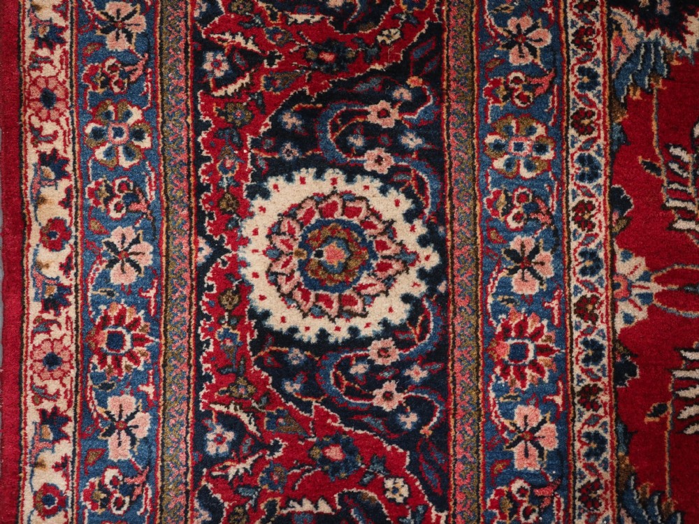 A large hand-knotted Kashan wool carpet featuring an intricate all-over floral pattern on a rich red field framed by a navy blue patterned border. View VIII