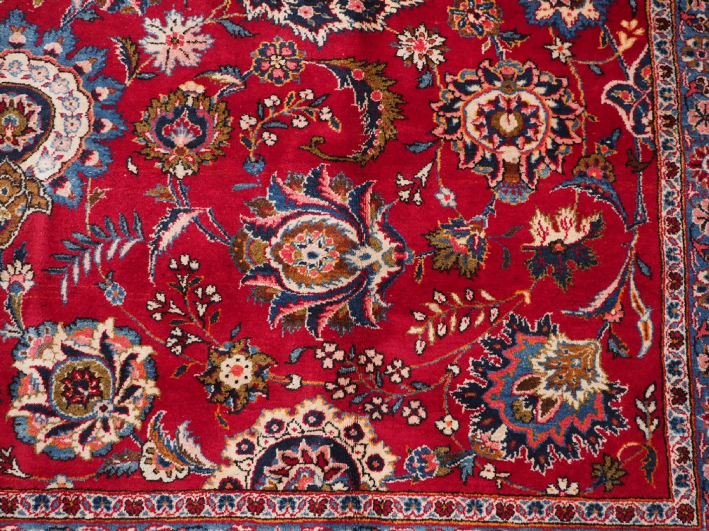 A large hand-knotted Kashan wool carpet featuring an intricate all-over floral pattern on a rich red field framed by a navy blue patterned border. View XIII
