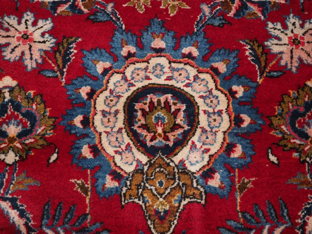 A large hand-knotted Kashan wool carpet featuring an intricate all-over floral pattern on a rich red field framed by a navy blue patterned border. View XIV