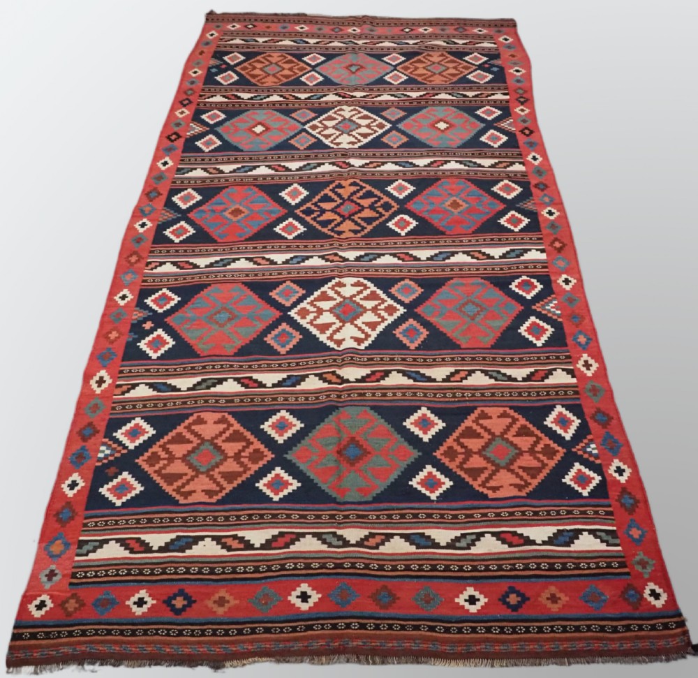 An antique Shahsavan wool flatweave kilim rug featuring geometric diamond motifs in red, navy blue, terracotta, and light blue tones.