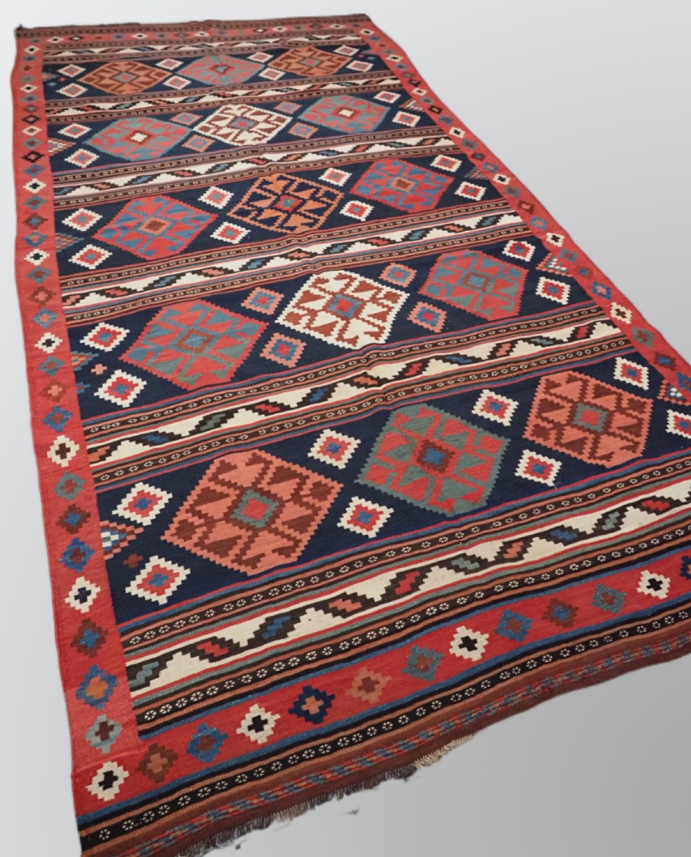 An antique Shahsavan wool flatweave kilim rug featuring geometric diamond motifs in red, navy blue, terracotta, and light blue tones. View II