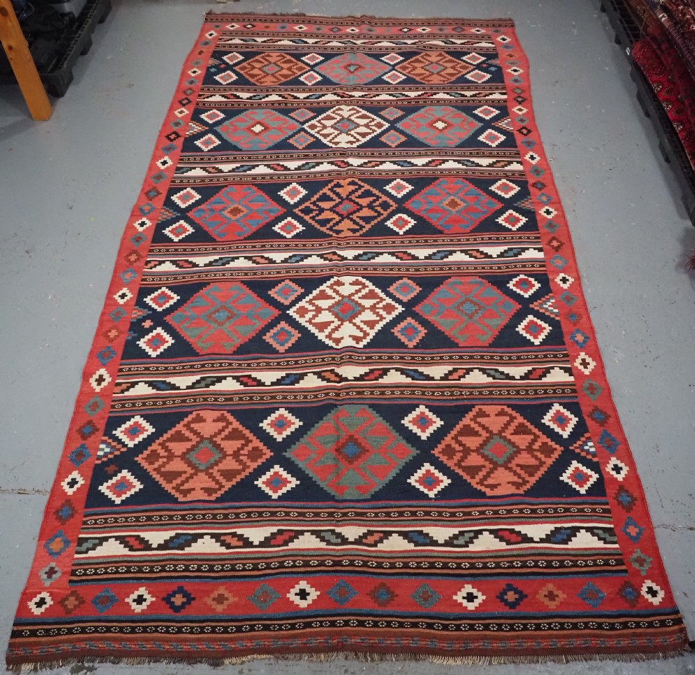 An antique Shahsavan wool flatweave kilim rug featuring geometric diamond motifs in red, navy blue, terracotta, and light blue tones. View III
