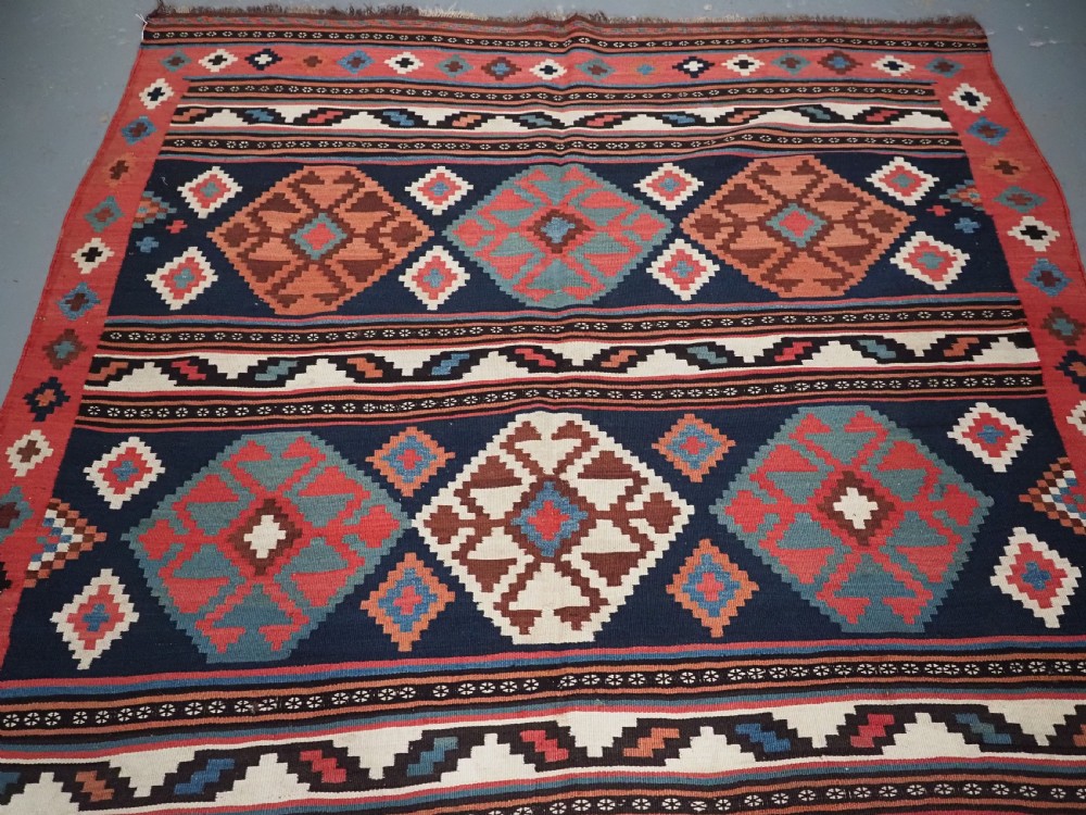 An antique Shahsavan wool flatweave kilim rug featuring geometric diamond motifs in red, navy blue, terracotta, and light blue tones. View IV