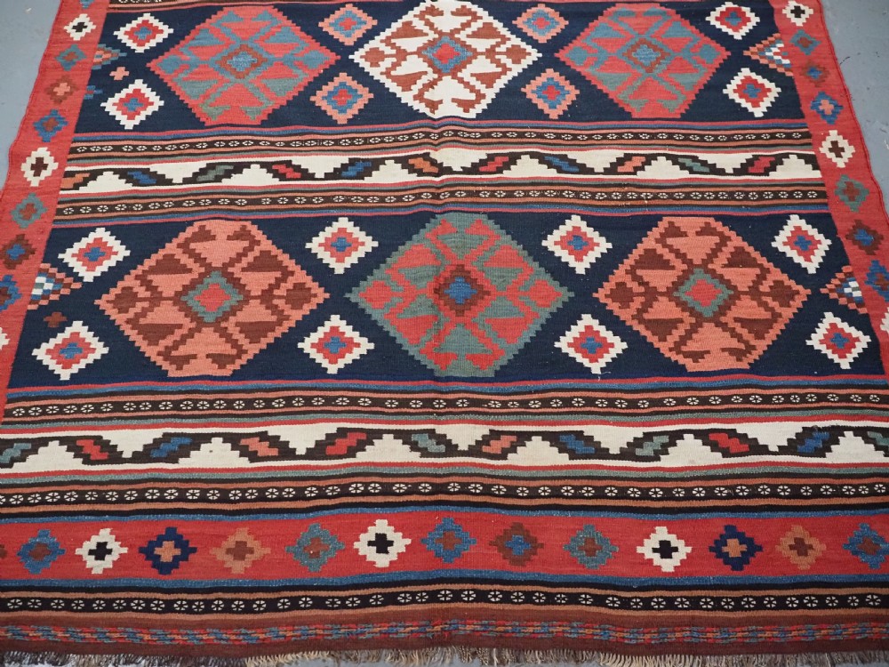 An antique Shahsavan wool flatweave kilim rug featuring geometric diamond motifs in red, navy blue, terracotta, and light blue tones. View VI
