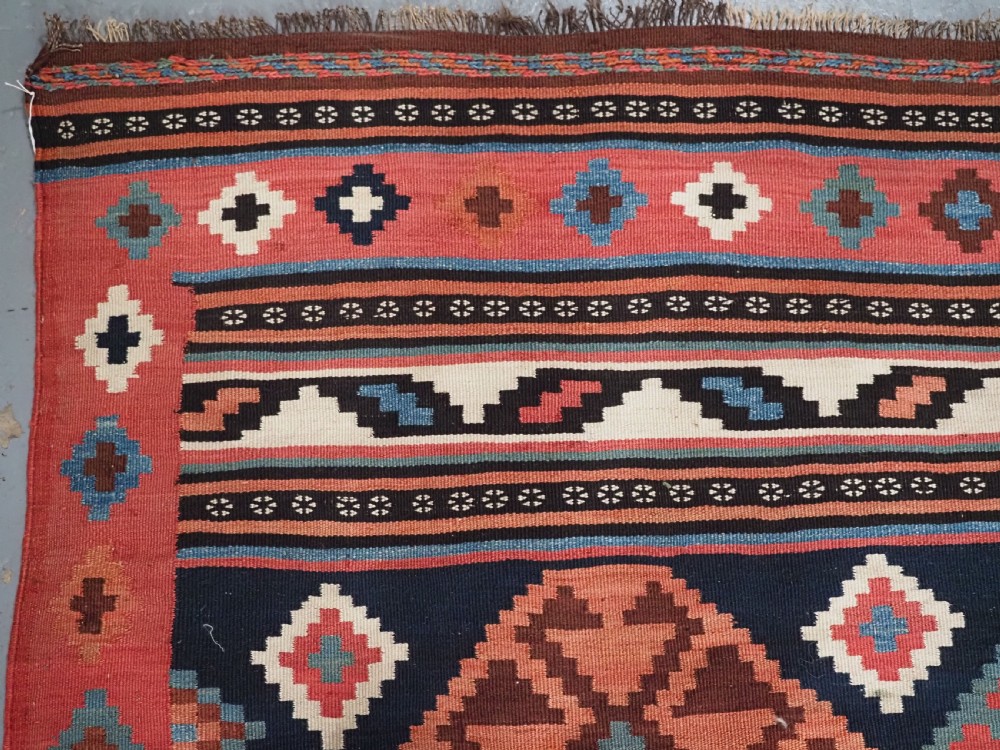 An antique Shahsavan wool flatweave kilim rug featuring geometric diamond motifs in red, navy blue, terracotta, and light blue tones. View VII