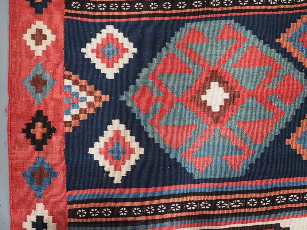 An antique Shahsavan wool flatweave kilim rug featuring geometric diamond motifs in red, navy blue, terracotta, and light blue tones. View VIII