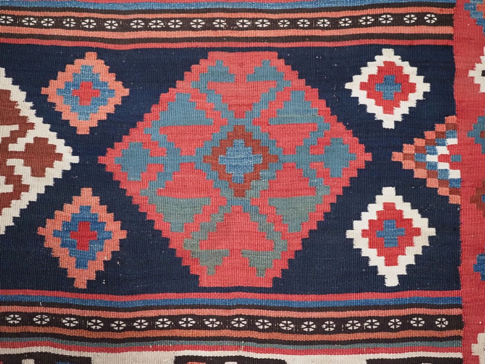 An antique Shahsavan wool flatweave kilim rug featuring geometric diamond motifs in red, navy blue, terracotta, and light blue tones. View XI