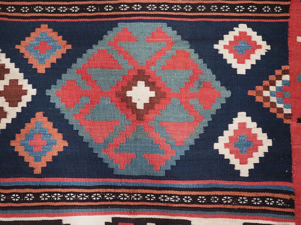 An antique Shahsavan wool flatweave kilim rug featuring geometric diamond motifs in red, navy blue, terracotta, and light blue tones. View XIII