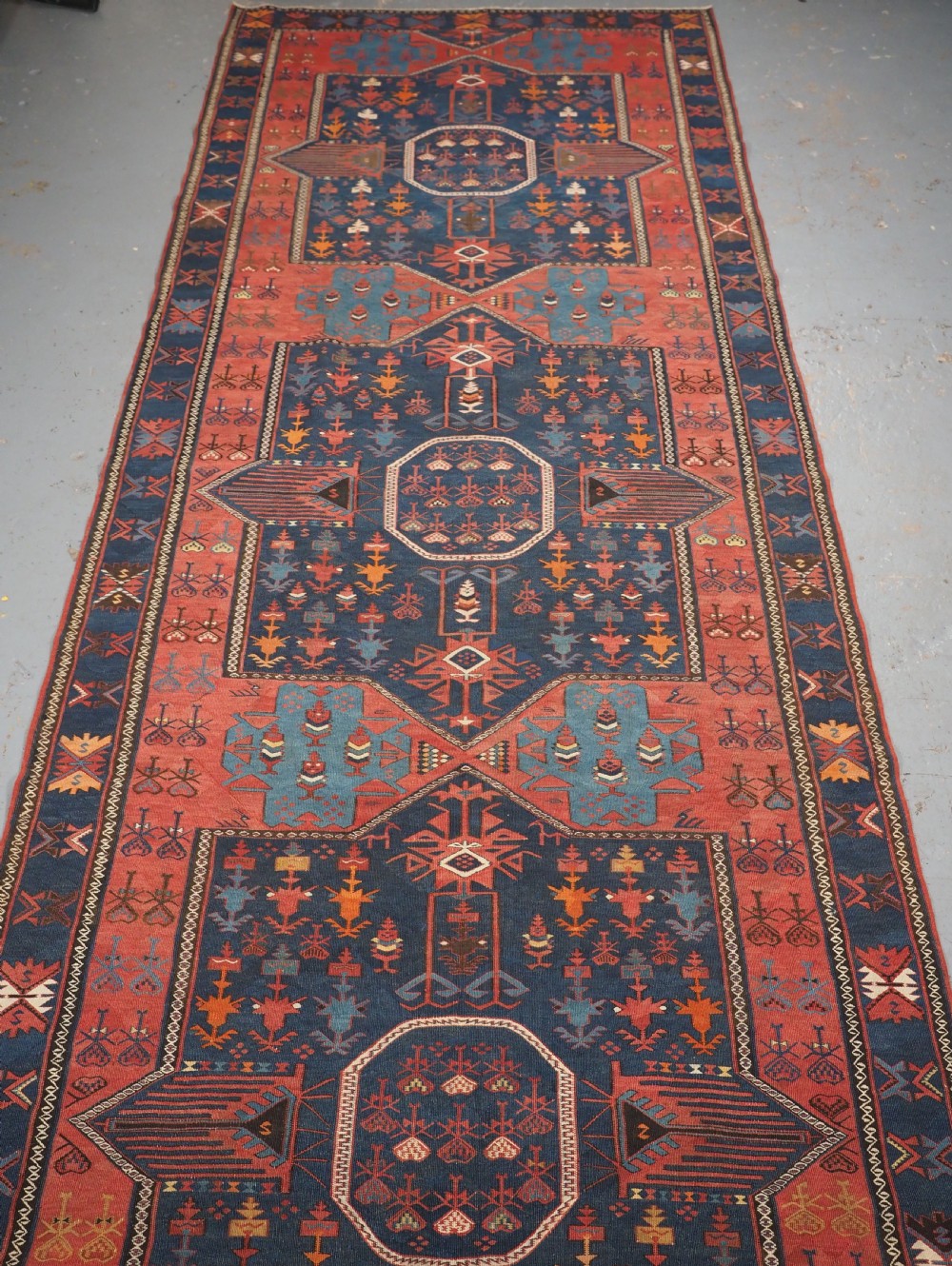An antique flatweave Caucasian Avar kilim runner featuring geometric octagonal medallions down a navy centre field framed by terracotta and blue patterned borders.