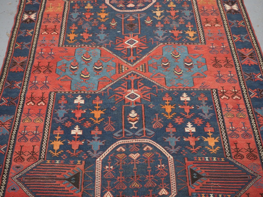 An antique flatweave Caucasian Avar kilim runner featuring geometric octagonal medallions down a navy centre field framed by terracotta and blue patterned borders. View V