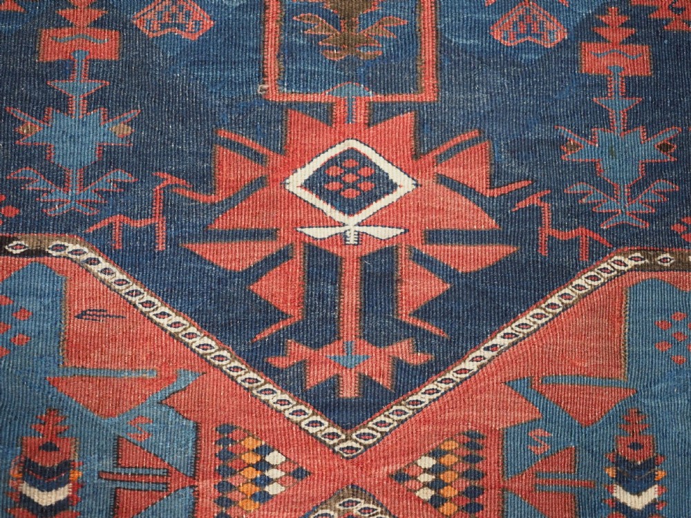 An antique flatweave Caucasian Avar kilim runner featuring geometric octagonal medallions down a navy centre field framed by terracotta and blue patterned borders. View X