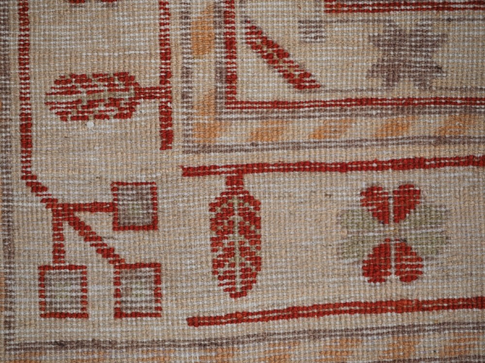 An antique East Turkestan Khotan wool area rug featuring three light blue geometric star medallions on a red field within wide cream and beige patterned borders. View X